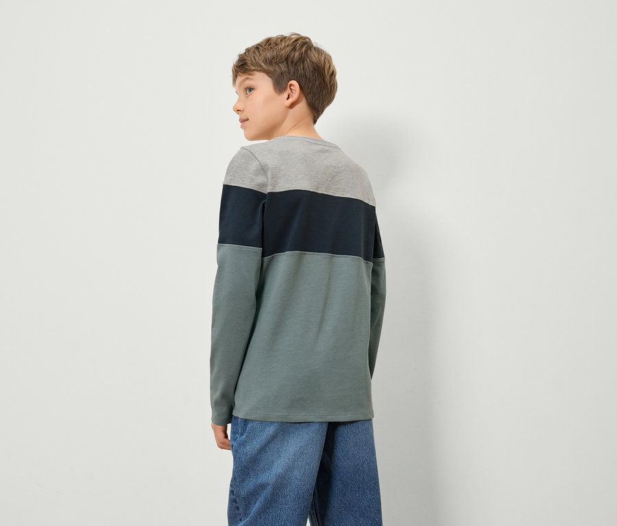 Un garçon portant un t-shirt coloré à manches longues et un jean, dos à la caméra.