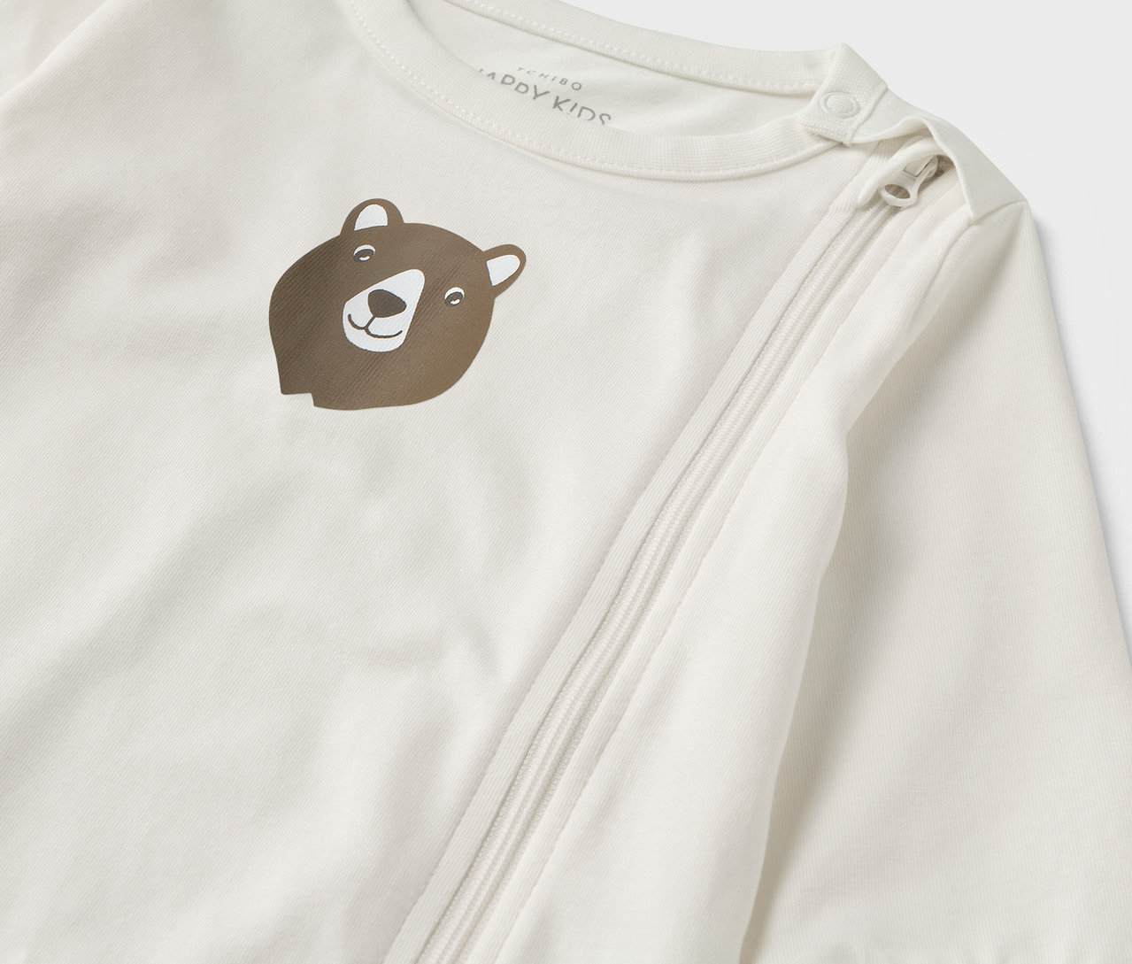 Gros plan sur un pyjama bébé blanc avec un motif d'ours brun et une fermeture éclair.