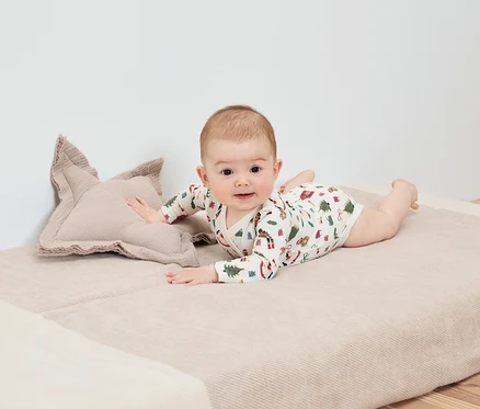 Bébé allongé sur le ventre sur une couverture à côté d'un coussin en forme d'étoile.