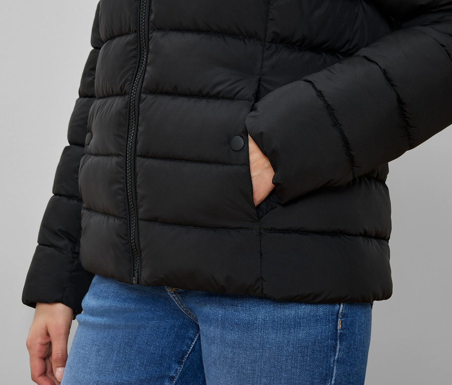 Personne portant une doudoune noire avec la main dans la poche et un jean bleu.