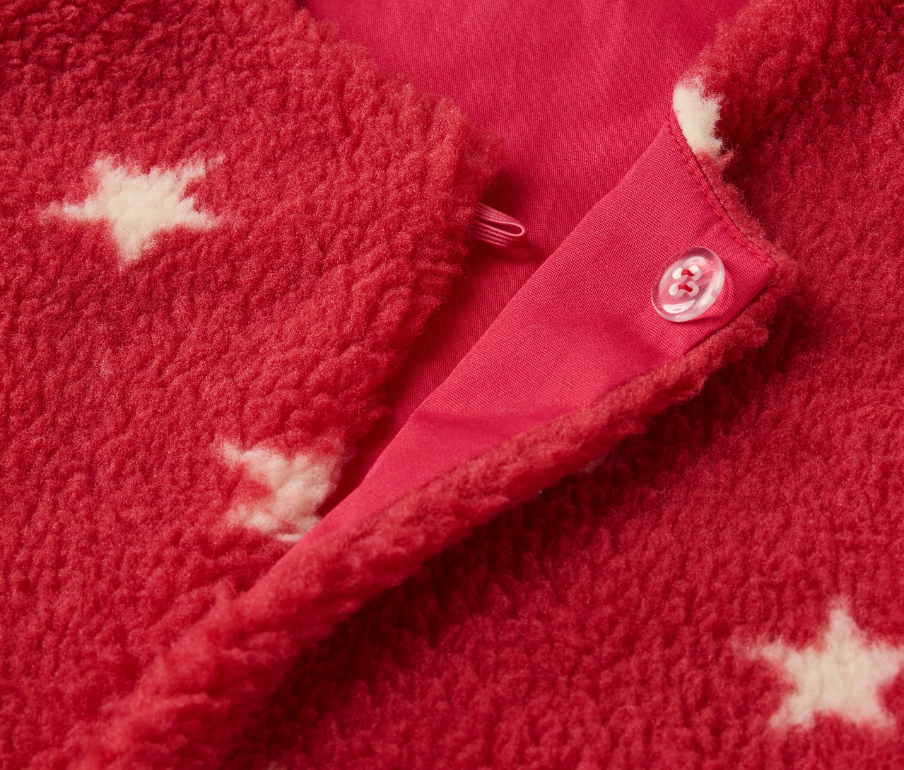 Détail d'un gilet sans manches enfant en polaire teddy rouge avec des étoiles blanches et une fermeture à bouton.