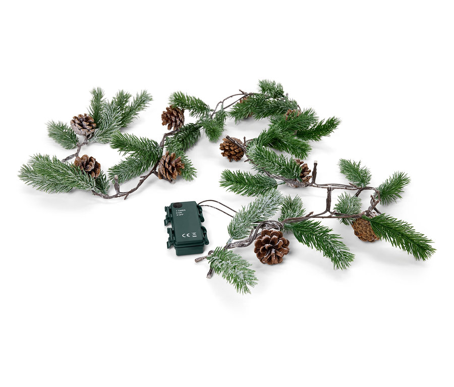 Une guirlande verte avec des pommes de pin et un boîtier à piles repose sur un fond blanc.