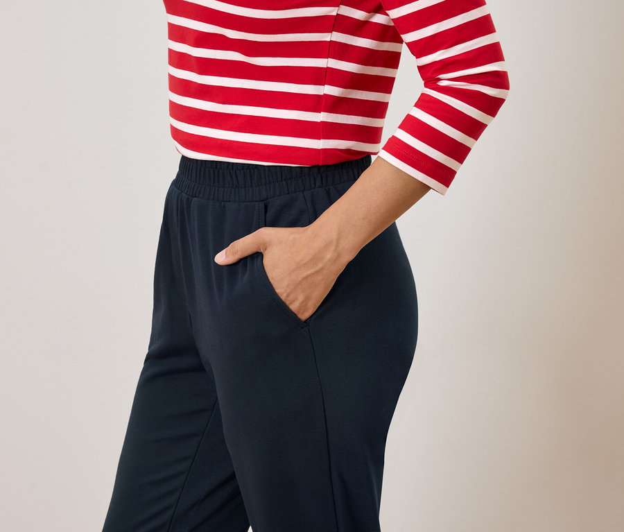 Femme avec la main dans la poche d'un pantalon bleu marine et un haut rayé rouge et blanc.