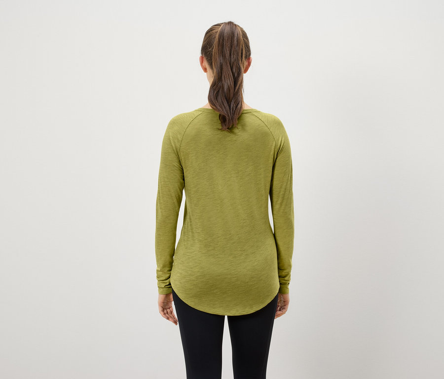 Vue de dos d'une femme aux cheveux bruns attachés en queue de cheval, portant un T-shirt à manches longues vert olive et un legging noir.
