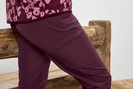 Pantalon bordeaux avec poches sur les cuisses appuyé contre un banc en bois.