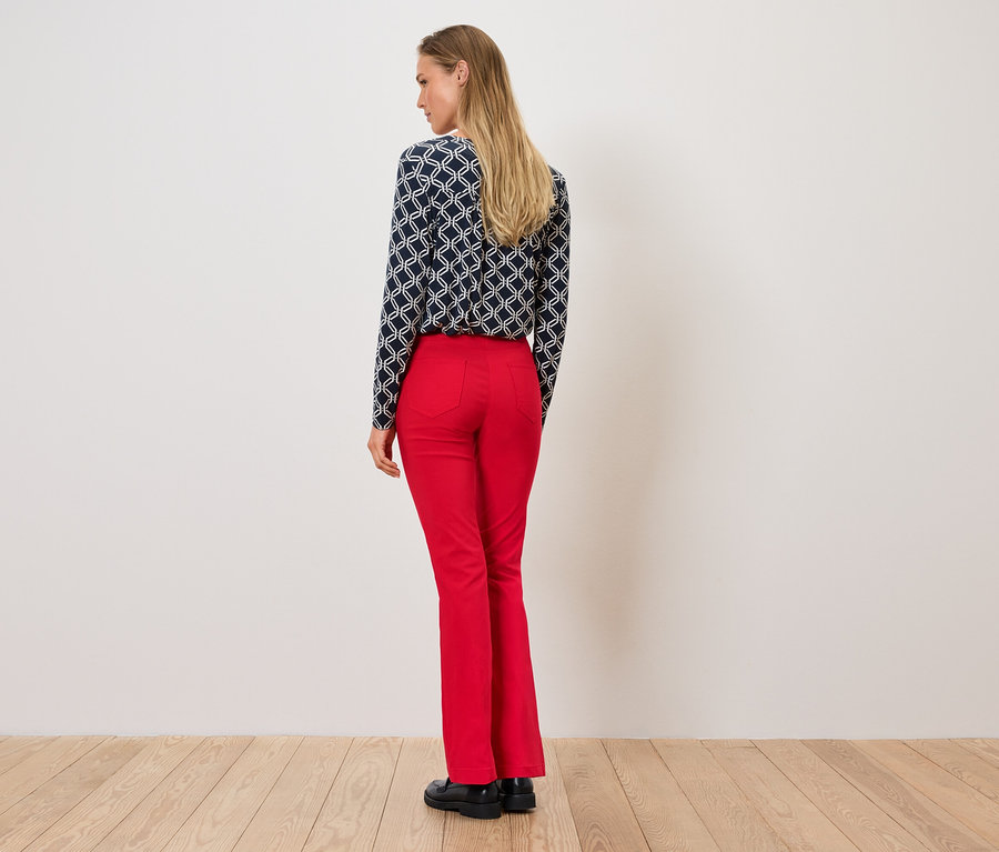 Une femme, vue de dos, porte un chemisier à motifs et un pantalon rouge.