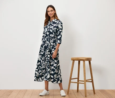 Une femme se tient à côté d'un tabouret en bois et porte une robe bleu marine à fleurs blanches.