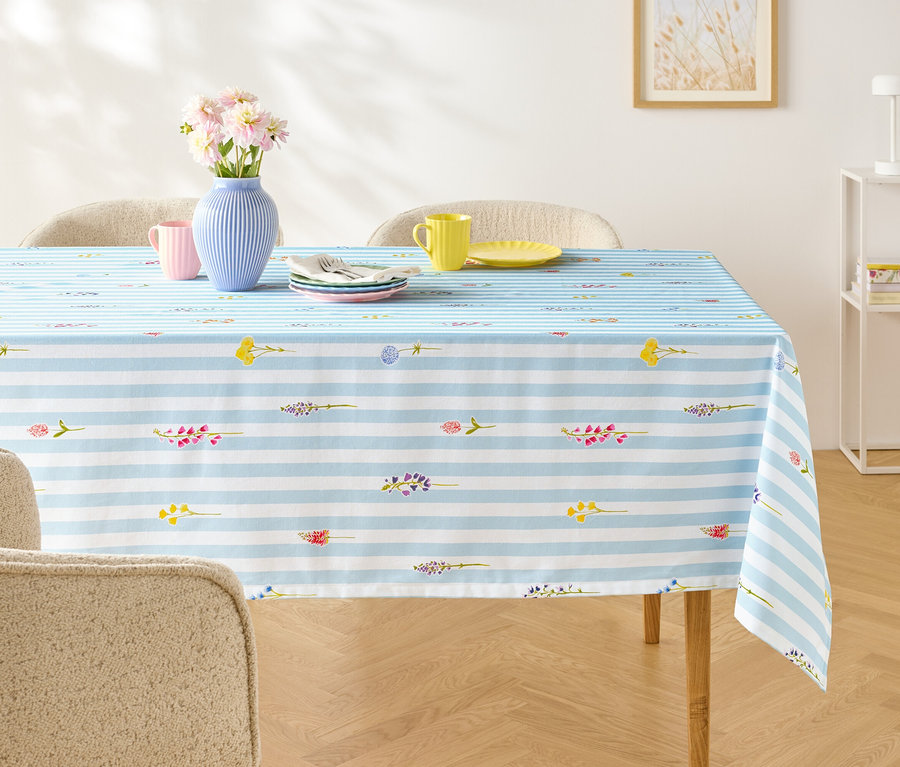 Table à manger avec une nappe à rayures bleues et blanches, sur laquelle sont posés de la vaisselle, des couverts et un vase de fleurs.