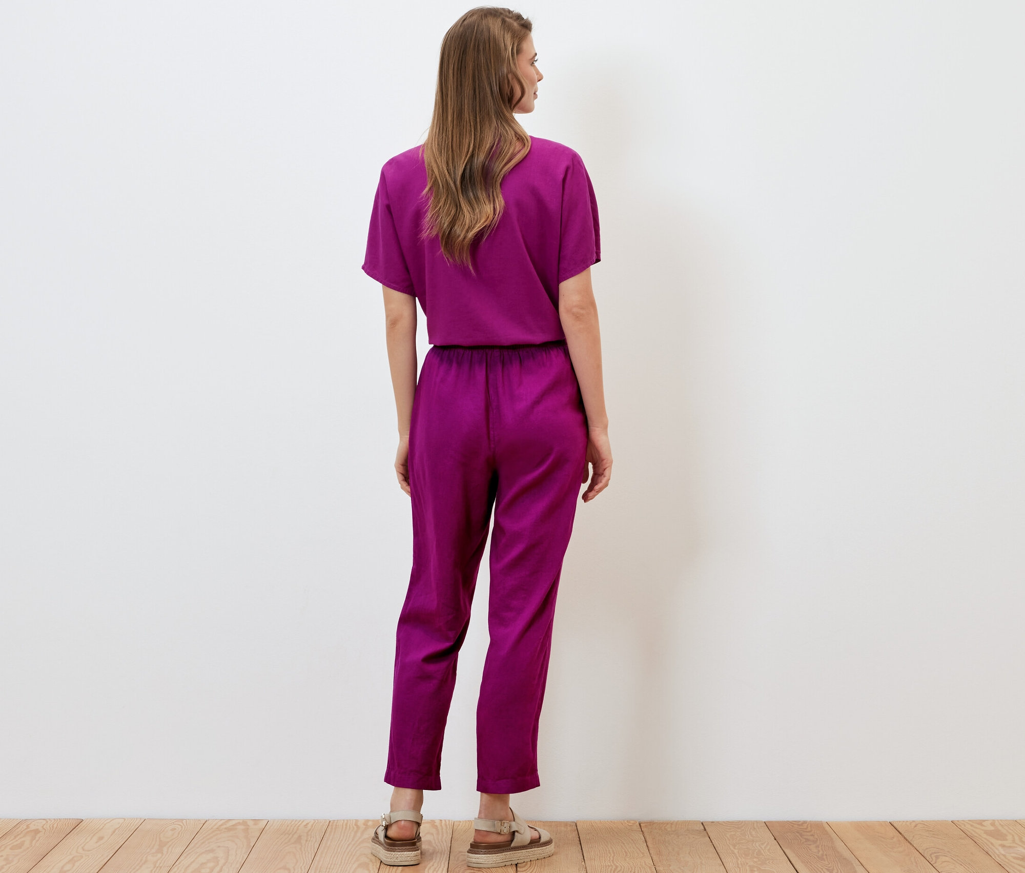 Une femme, vue de dos, porte un pantalon en lin rouge baie.