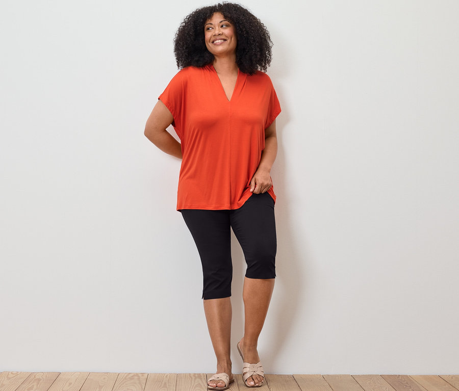 Femme posant en blouse orange à encolure en V et pantalon 3/4 stretch noir.