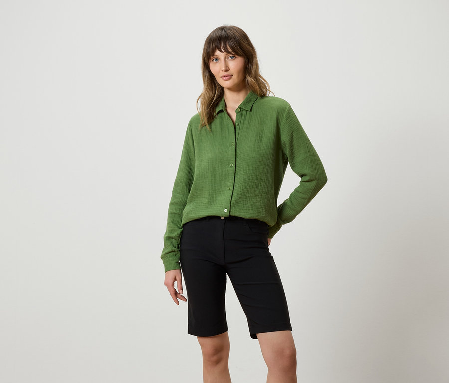 Une femme portant une chemise verte et un short noir pose devant un fond blanc.