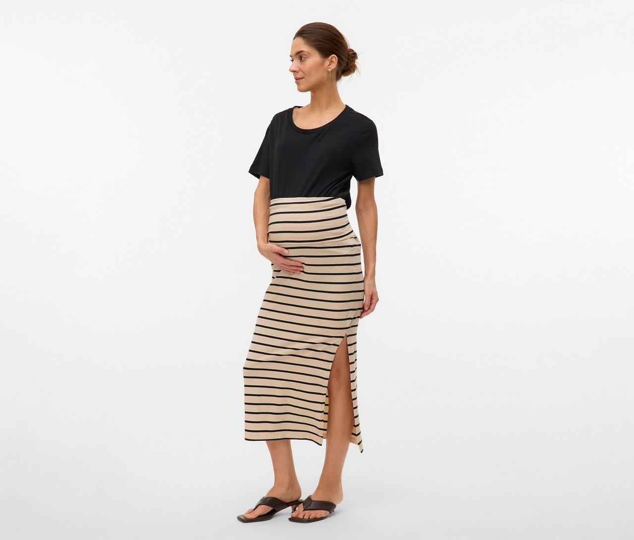 Femme portant un t-shirt noir et une jupe longue rayée MAMALICIOUS «
MLEVA
» avec une fente. Elle tient ses mains sur son ventre.