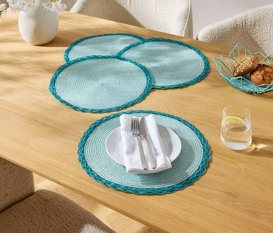Une table à manger avec quatre sets de table turquoise, une assiette avec des couverts, un verre d'eau, un vase de fleurs et une corbeille de pain.