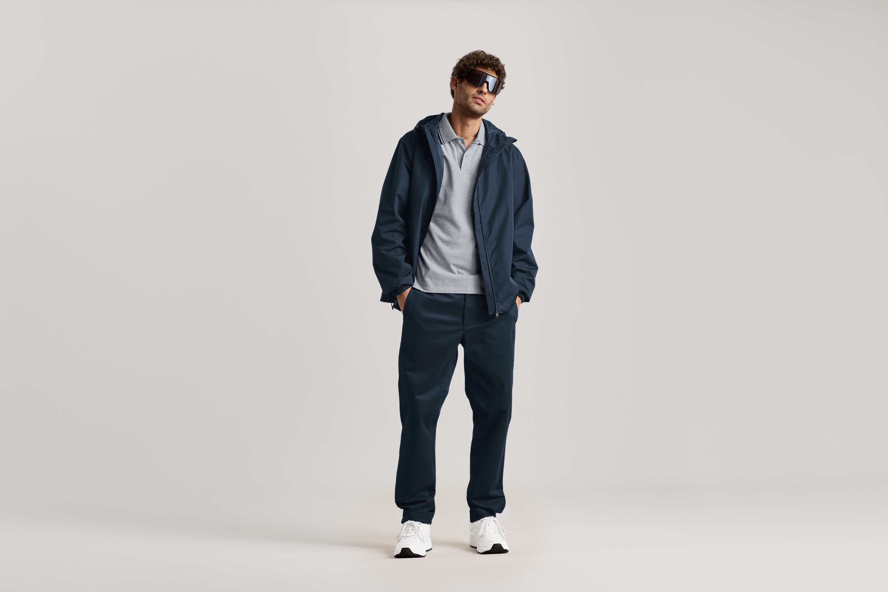 Un homme se tient debout avec des lunettes de soleil, une veste bleu marine et un chino bleu marine.