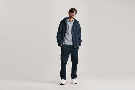 Un homme se tient debout avec des lunettes de soleil, une veste bleu marine et un chino bleu marine.