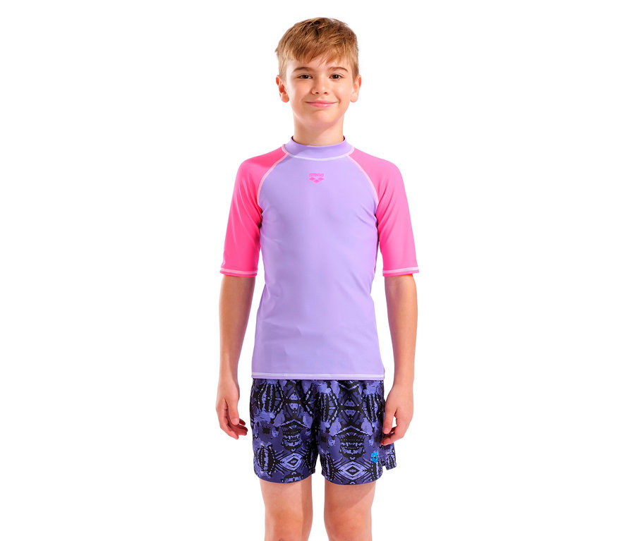 Un jeune homme porte un t-shirt violet avec des manches roses et un short de bain à motifs.