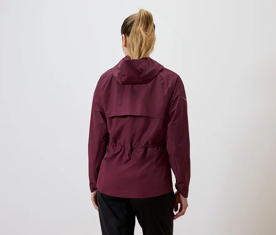 Vue arrière d'une femme avec une queue de cheval blonde portant une veste bordeaux à capuche avec cordon de serrage à la taille et un pantalon noir.