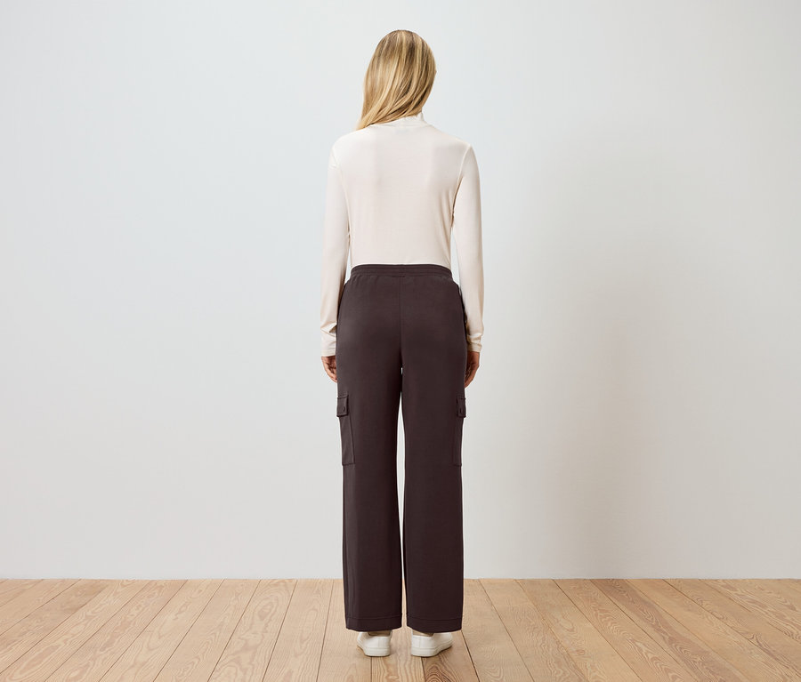 Vue arrière d'une femme blonde portant un pull à col roulé crème, un pantalon cargo marron et des baskets blanches.