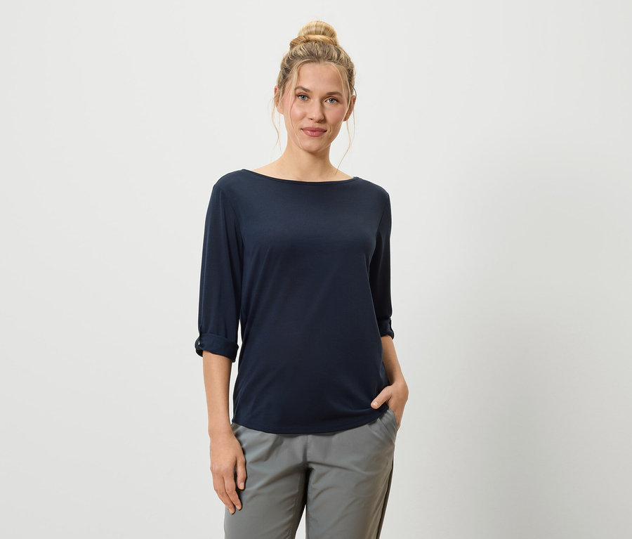 Une femme avec un chignon porte un t-shirt bleu marine et un pantalon gris.
