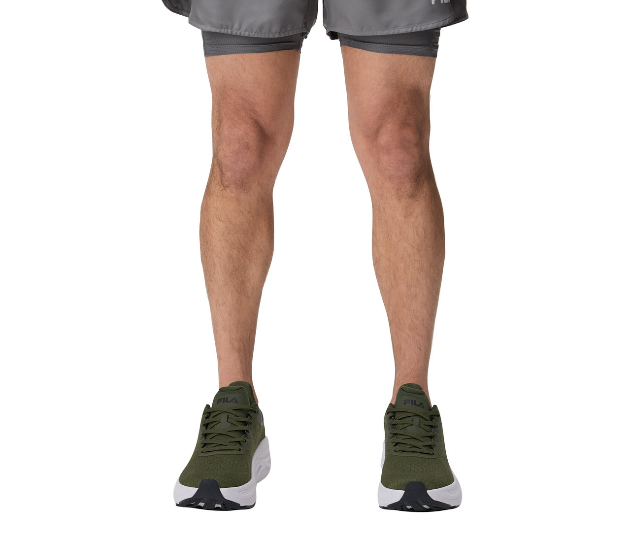 Jambes d'une personne portant un short de sport FILA pour hommes et des baskets vertes.