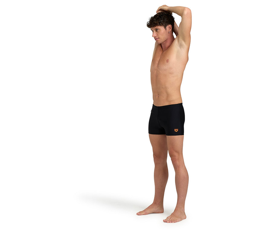 Un homme s'étire et porte un short de bain noir.