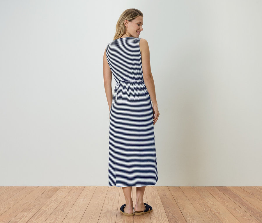 Femme vue de dos portant une robe maxi sans manches à rayures bleues et blanches et des sandales.