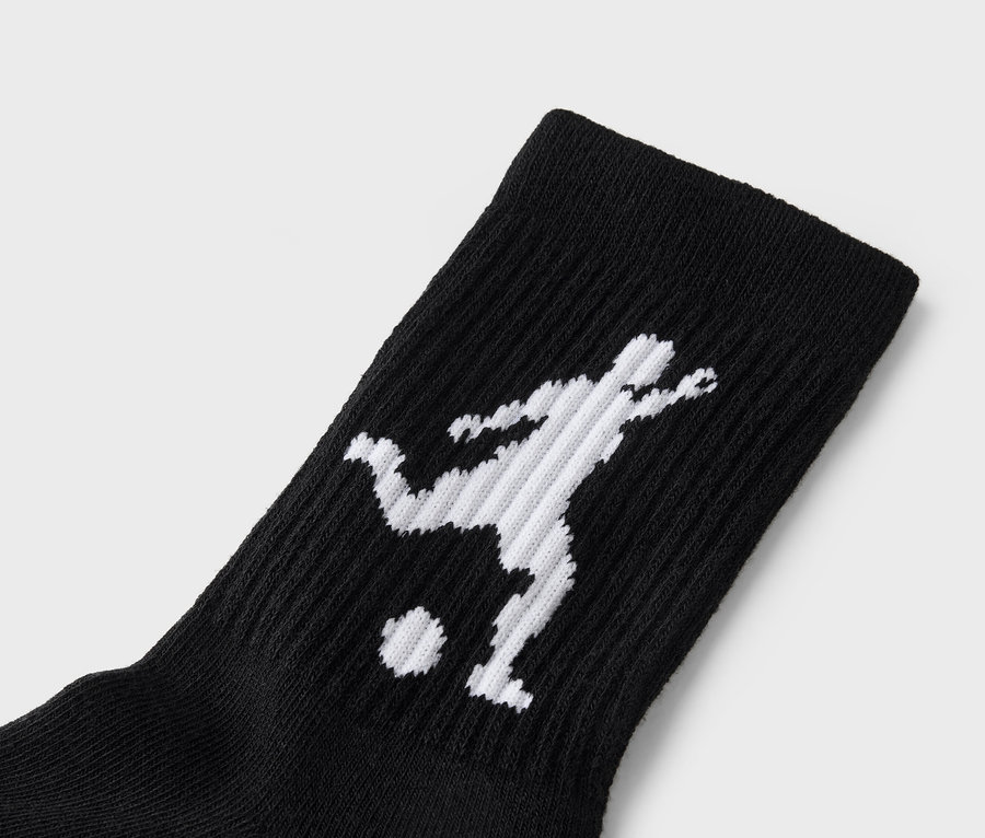Gros plan d'une chaussette noire avec une silhouette blanche d'un joueur de football donnant un coup de pied dans un ballon.