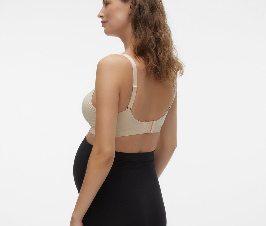 Femme enceinte de profil, portant un soutien-gorge couleur chair et un legging noir.