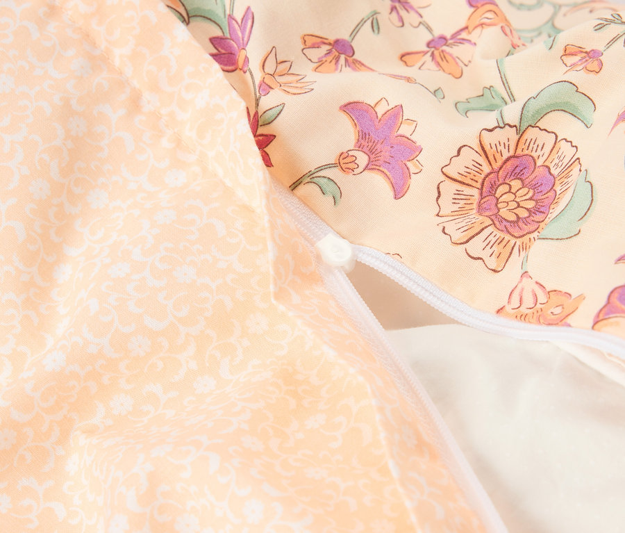Gros plan d'un coussin avec une fermeture éclair. Le coussin a un motif floral dans les tons de jaune, d'orange et de violet.