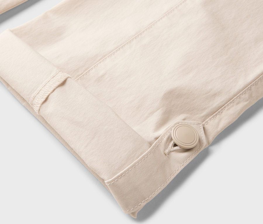 Gros plan sur la manche d'une chemise beige, retroussée et fixée par un bouton.