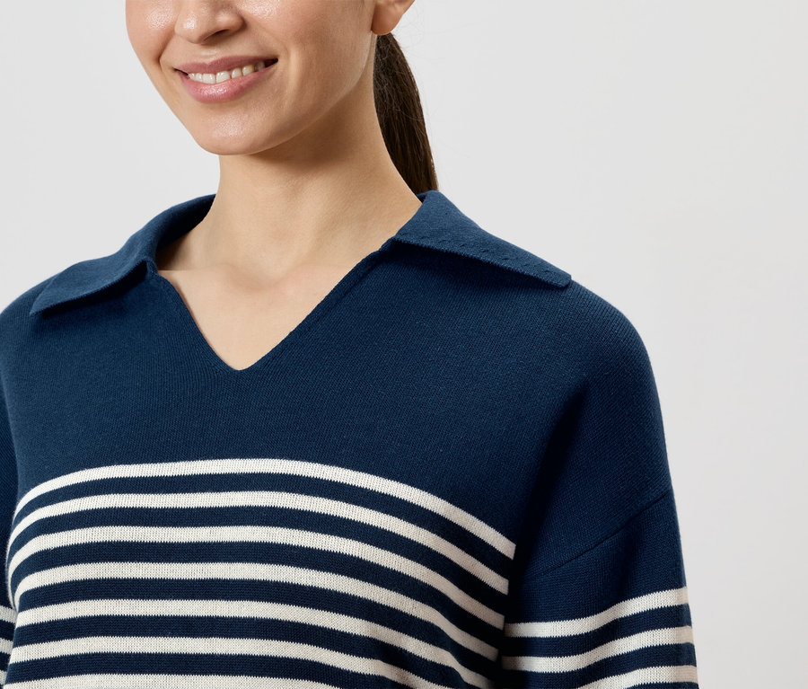 Une femme souriante porte un polo bleu marine rayé avec un col.