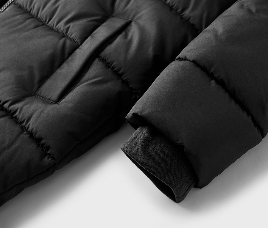Gros plan d'une doudoune noire matelassée avec un poignet côtelé et une poche visible.
