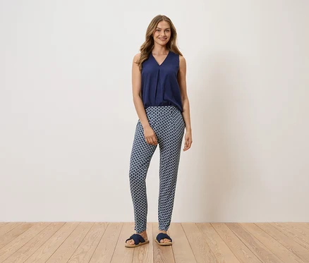 Femme debout portant un haut bleu marine, un pantalon à motifs et des sandales.
