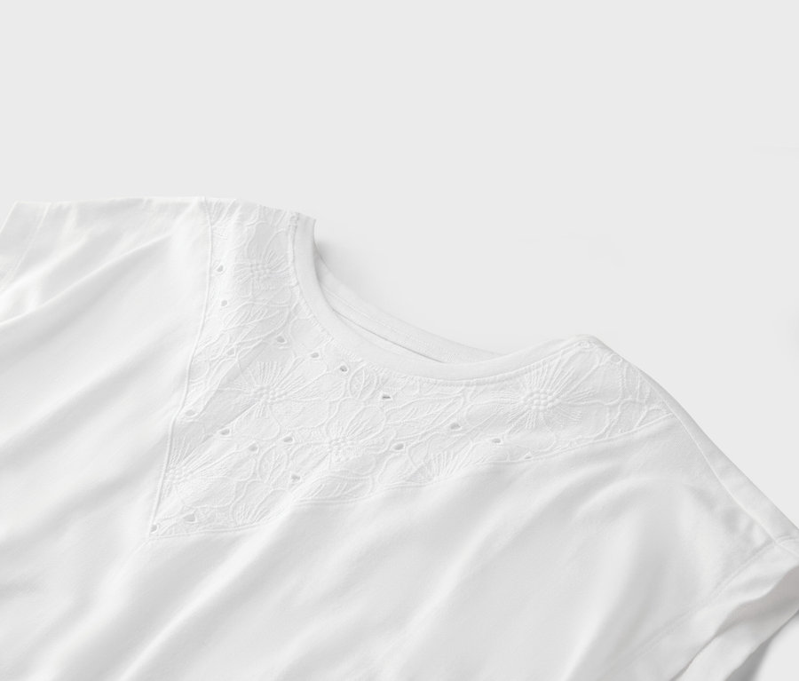 Gros plan sur un t-shirt blanc avec des broderies ajourées à l'encolure.