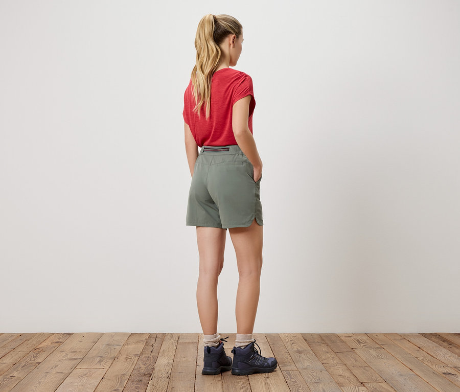 Femme de dos portant un t-shirt rouge, un short et des chaussures de randonnée.