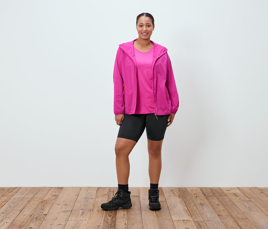 Femme debout portant une veste rose, un t-shirt rose, un short noir, des chaussettes noires et des bottes noires.