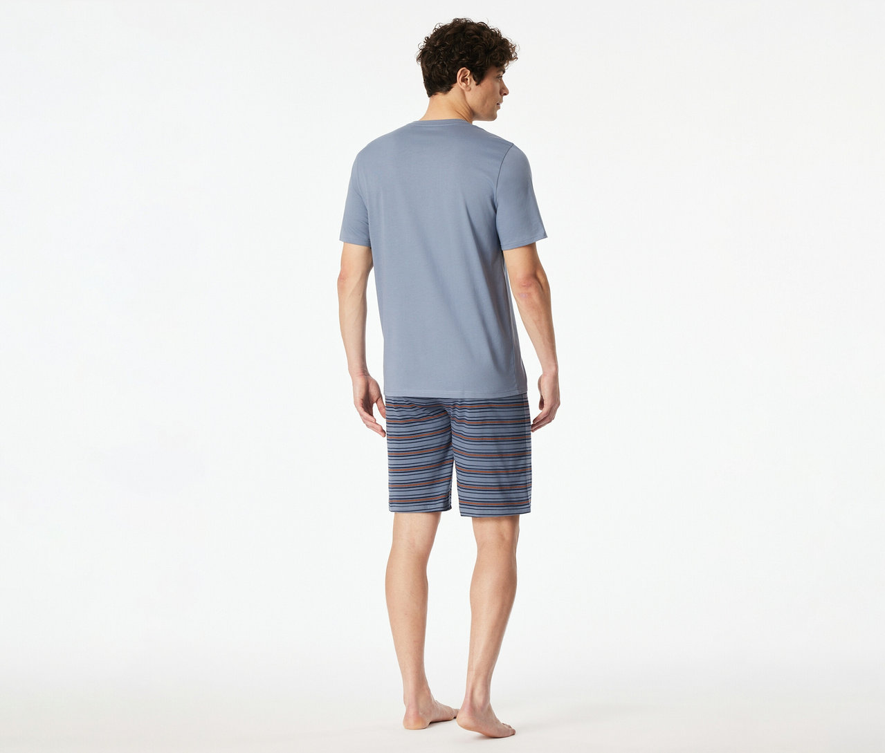 Un homme vu de dos, portant un t-shirt bleu clair à manches courtes et un short rayé du set shorty SCHIESSER. Il est pieds nus.