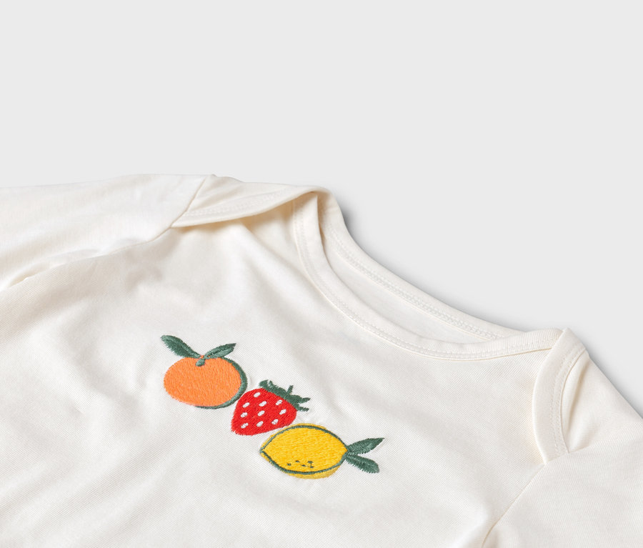 Gros plan sur un body blanc pour bébé avec une mandarine, une fraise et un citron brodés.