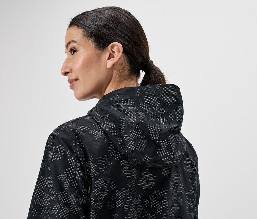 Une femme avec une queue de cheval, vue de dos, porte un imperméable noir à capuche avec un motif floral.