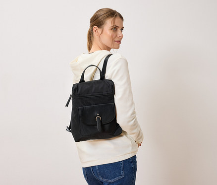 Femme portant un sac à dos noir, debout devant un fond blanc.