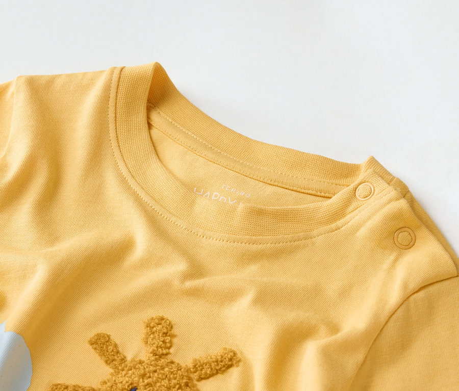 Gros plan sur un t-shirt pour enfant jaune doré avec une application de girafe et un motif de nuage.