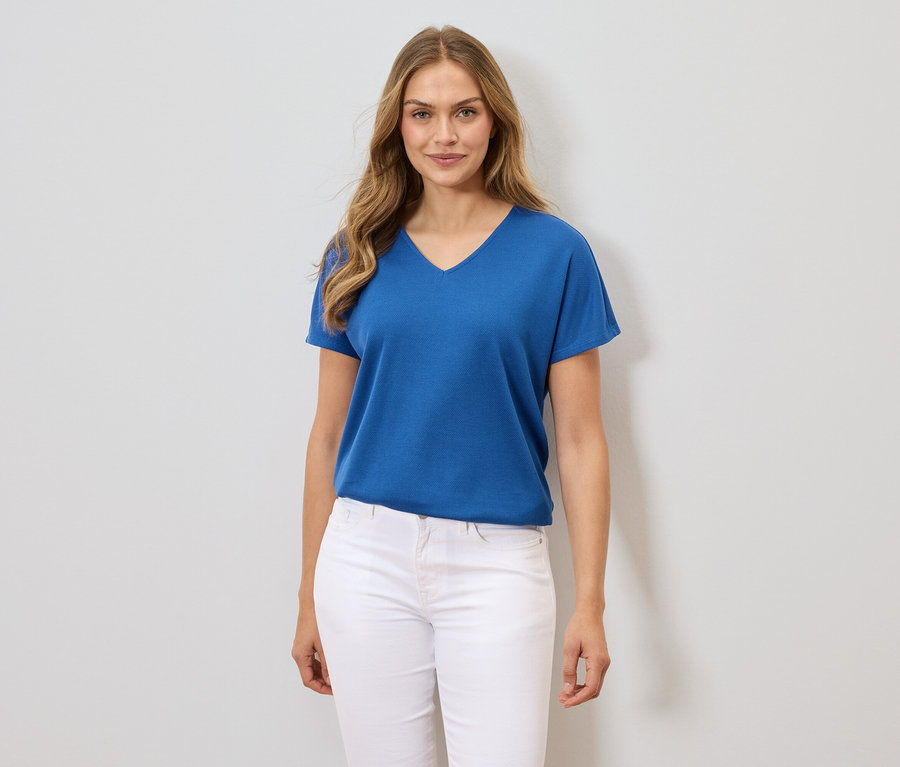 Une femme porte un t-shirt bleu et un pantalon blanc.