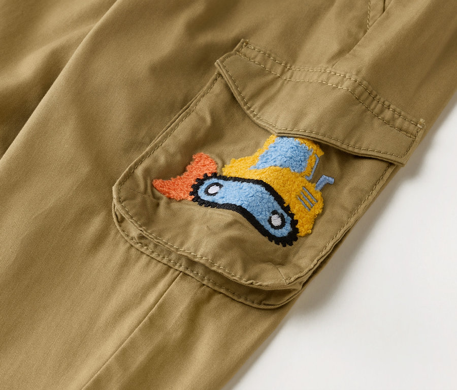 Gros plan sur un pantalon cargo kaki avec une poche plaquée ornée d'une pelleteuse brodée en orange, jaune et bleu.