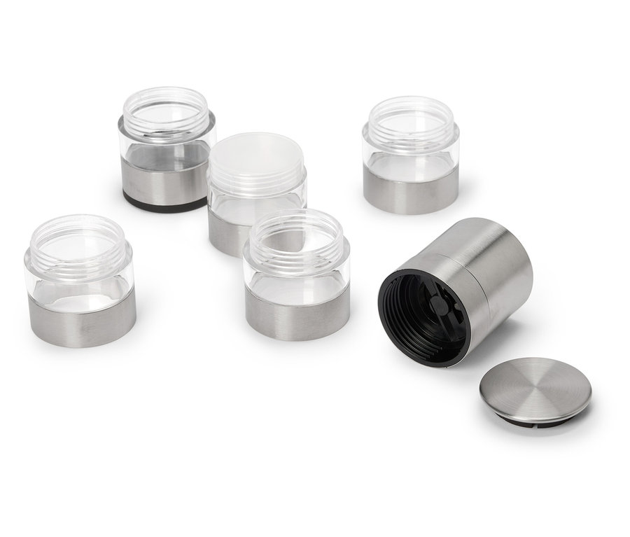 Six pots à épices, certains avec des couvercles en métal, certains ouverts, sont posés sur un fond blanc.