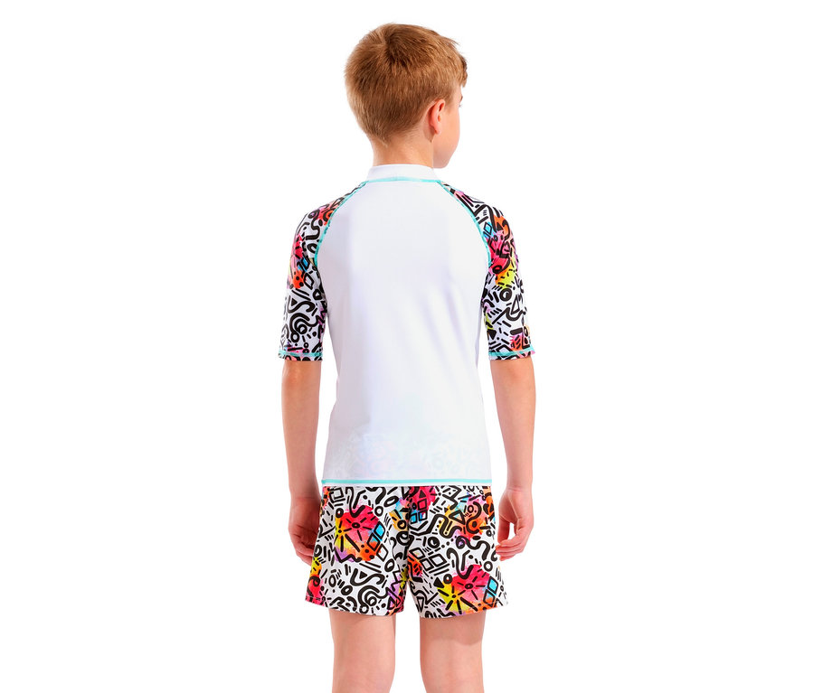 Garçon vu de dos portant un haut Rash Guard blanc avec des manches colorées et un short coloré à motif graphique.