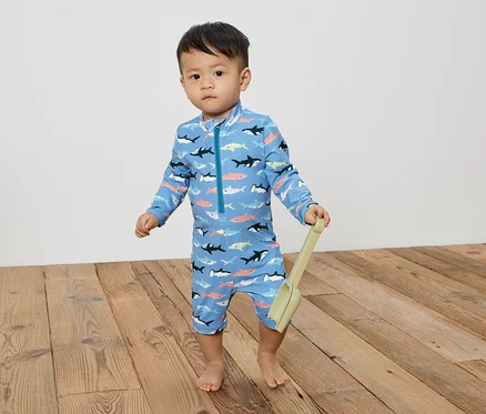 Petit garçon en maillot de bain bleu à motifs de requins tenant une pelle.