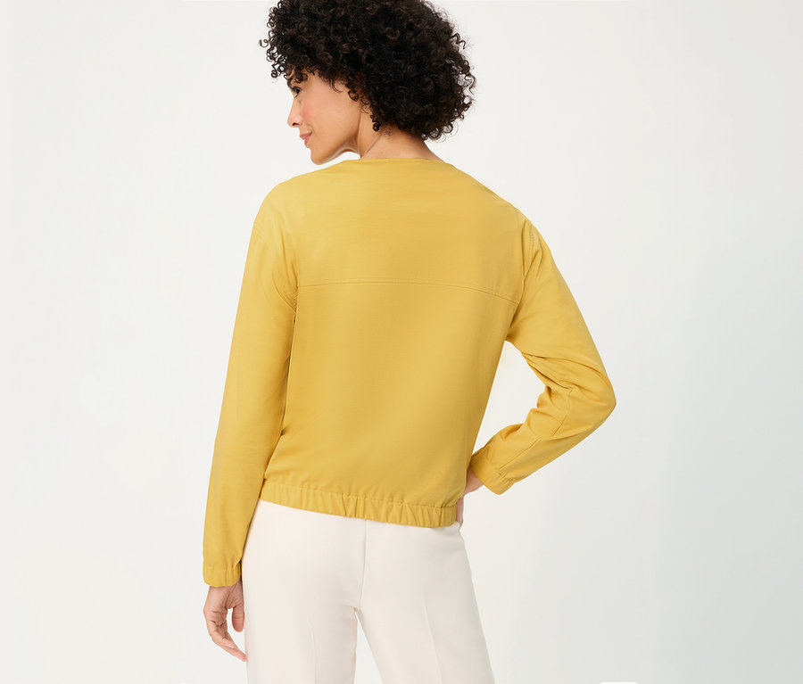Femme de dos portant une veste de survêtement Olsen jaune et un pantalon clair.