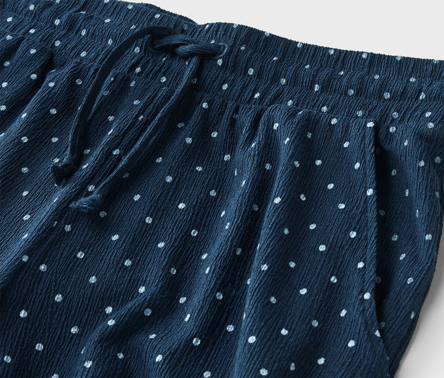Gros plan d'un pantalon bleu marine à pois blancs avec cordon de serrage et taille élastique.