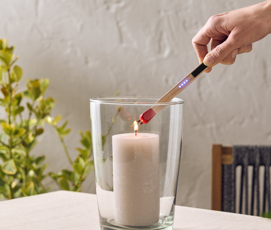 Une main allume une bougie dans un verre avec un briquet à arc. Le verre est posé sur une table.