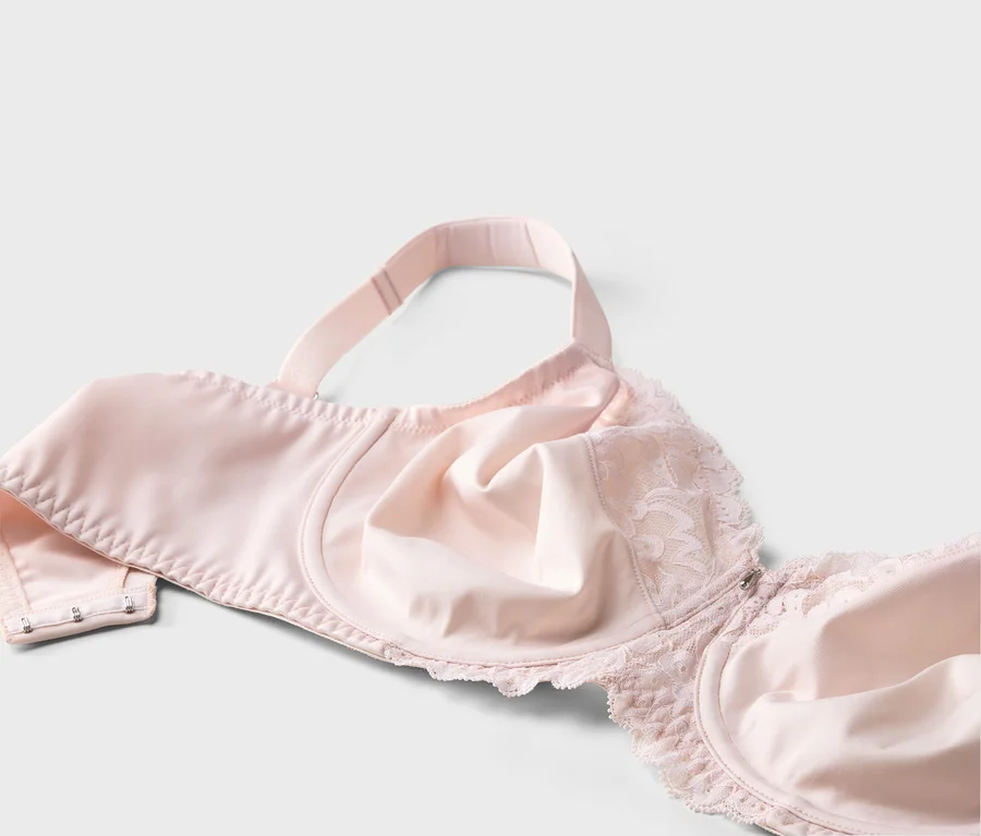 Gros plan d'un soutien-gorge rose clair avec de la dentelle et des bretelles réglables sur fond blanc.